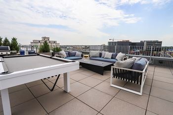 A white table and a sofa with cushions are on a rooftop patio. at RiDE at RiNo Apartments, Denver, CO